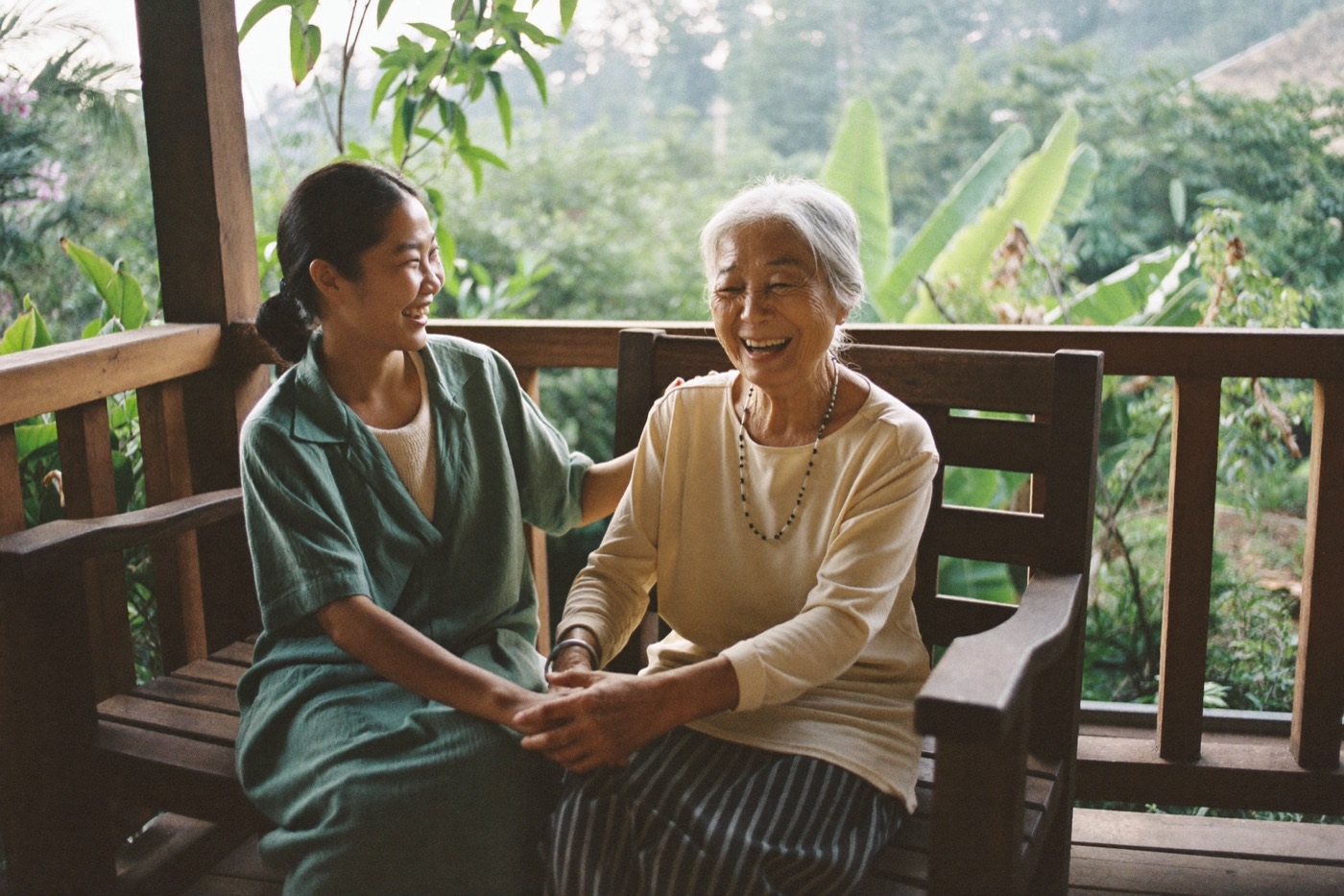 A caregiver chatting with an elderly woman on a wooden bench in a tropical garden